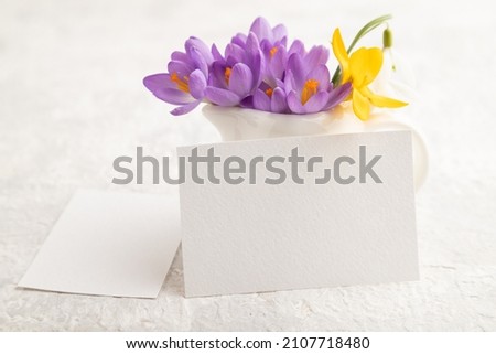White paper business card mockup with spring snowdrop crocus and galanthus flowers on gray concrete background. Blank, business card, side view, copy space, still life. spring concept.