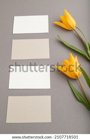 White and beige business cards and orange tulip flowers on gray pastel background. side view, copy space, still life. Beauty, spring, summer concept.