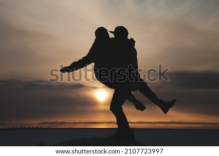 Silhouettes of a couple in love in winter against the background of the setting sun. A guy and a girl have fun on a romantic date in the cold