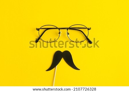 Father's Day Holiday Concept. Transparent glasses, stylish black paper photo booth props moustaches on yellow background. 