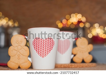 Two cups and gingerbread men on table with garlands blurred background. Kitchen is decorated for New Year. Interior details with Christmas decor.