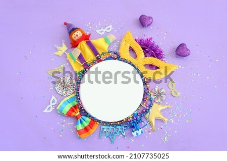 carnival party celebration concept with mask and colorful party accessories over purple wooden background. Top view