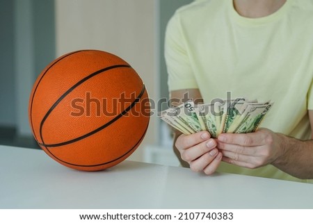 Lucky man with basketball ball counting dollar banknotes. Close up of male hands count money cash payout after win at basketball betting. Concept of betting, gambling.