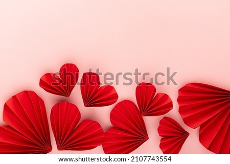 Sweet abstract love background for wedding or Valentines day with soar red paper ribbed hearts in oriental style on pink backdrop, top view, footer border, copy space. Royalty-Free Stock Photo #2107743554