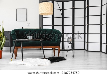 Interior of light living room with green sofa, table and lamps