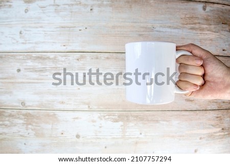 Hand holding a ceramic mug blank on wooden background with copy space, space for text