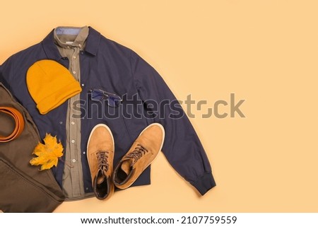 Stylish male jacket, pants, belt, hat, shoes, eyeglasses and autumn leaf on color background