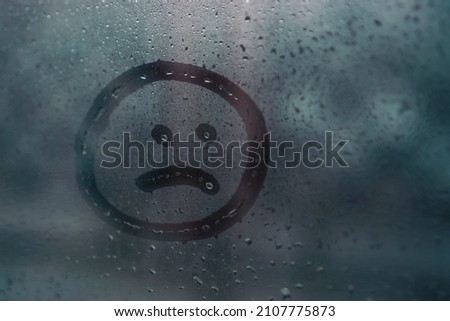 Sad smiley drawn by hand on wet fogged glass from the rain, copy the space. Concept of loneliness, sadness, bad weather Royalty-Free Stock Photo #2107775873
