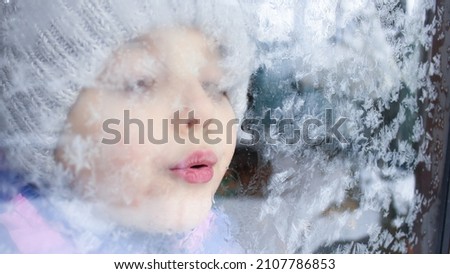 Frosty glass, pink lips blow on the glass, the frosty pattern melts, the child breathes.The weather is frost, cold, the breath of the north Royalty-Free Stock Photo #2107786853
