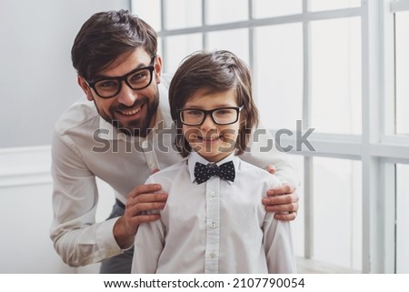Portrait of a handsome young father and his cute little son in a bow tie. Both in white classical shirts and eyeglasses, looking in camera and smiling