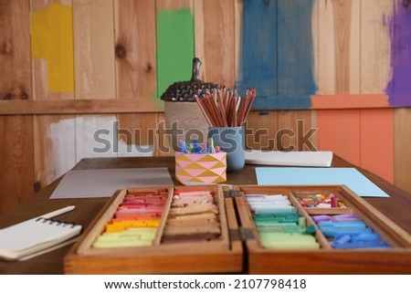 Blank sheets of paper, colorful chalk pastels and drawing pencils on wooden table indoors. Modern artist's workplace