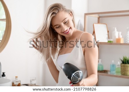 Pretty young woman blow drying her hair in bathroom Royalty-Free Stock Photo #2107798826
