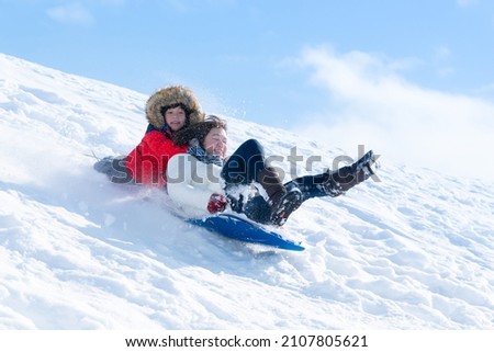 Asian mother and her son  sliding on sleds down snow hill in winter
