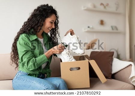 Delivery Concept. Happy Female Buyer Holding Footwear Unpacking Cardboard Box Sitting On Couch At Home. Joyful Customer Woman Receiving Shoes After Successful Online Shopping Royalty-Free Stock Photo #2107810292