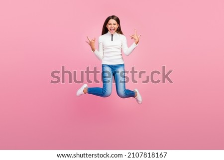 Full body photo of cool brunette small girl jump show rock sign wear sweater jeans footwear isolated on pink color background