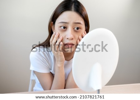 Sleepless Asian woman looking her face in the mirror and worry about dark circles under eyes Royalty-Free Stock Photo #2107821761