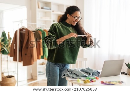 Happy Female Designer Or Fashion Blogger Taking Photo Of Garment On Phone Working In Modern Showroom Indoors. Fashion Entrepreneurship And Blogging, Design And Technology Concept Royalty-Free Stock Photo #2107825859