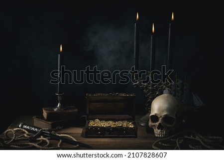 Treasure chest with a gold coins,dagger and human skull on a pirate captain table in the light of burning candles. Royalty-Free Stock Photo #2107828607