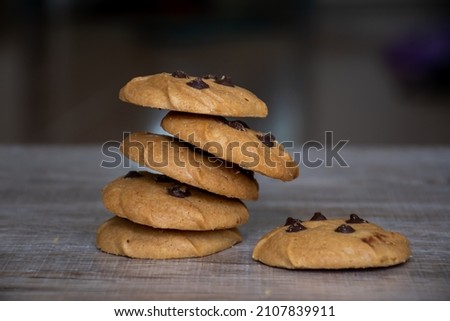 Picture shows chocolate chip cookies stacked on a wooden board.
