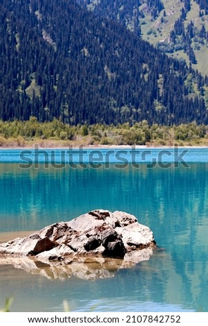 scenic view of the mountain lake and the slopes of the mountains covered with fir trees in sunny summer day. Vertical photo of Issyk lake in Kazakhstan.