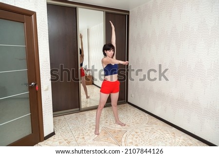 slender brunette woman in shorts and a tank top mirror is doing gymnastics while on self-isolation remote work.