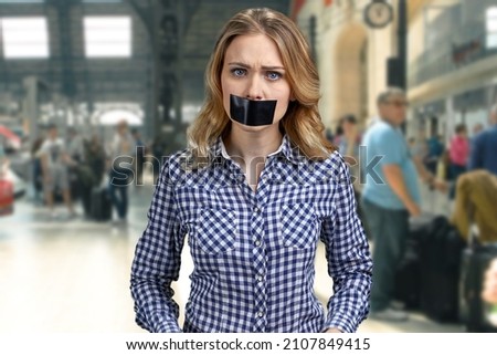Female protestor with black tape over her mouth demonstrating protest on blurred background. Royalty-Free Stock Photo #2107849415