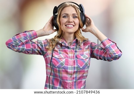 Happy young woman with headphones on abstract blurred background.