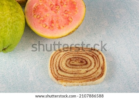 A slice of bolo de rolo on a blue and white background, next to guavas.