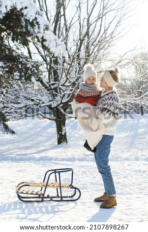 Young mother and her cute little son with retro sled in a snowy park during sunny winter day