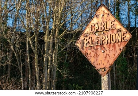 Vintage distressed Cable Telephone sign. Rusty, weathered, aged and unique. Stating "Cable Telephone", in a heavy bold metal font. Steampunk look metal plate with a woodland background. Orange brown 