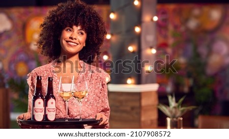 Portrait Of Smiling Female Server Holding Tray Of Drinks In Cool Bar Or Club Royalty-Free Stock Photo #2107908572