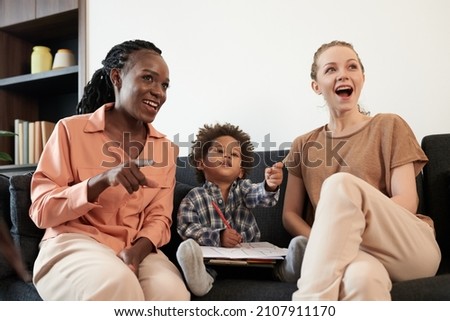 Multi-ethnic lesbian couple and their little son drawing and watching animated cartoon on tv at home