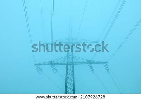 High voltage pylon with power lines in the fog.