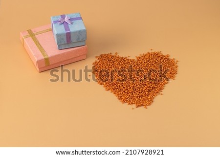 Heart shape with boxes of gifts on an orange background. The figurine is made of bright orange shiny beads. Valentine's day signs and symbols for copy space. Festive mockup.	