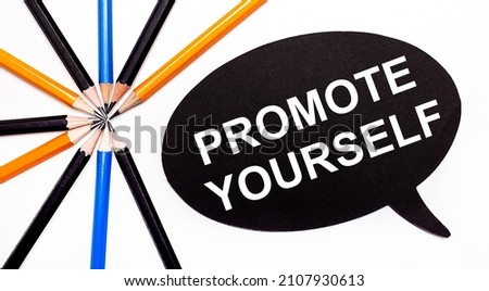 On a light background, multi-colored pencils and on a black background a white card with the text PROMOTE YOURSELF