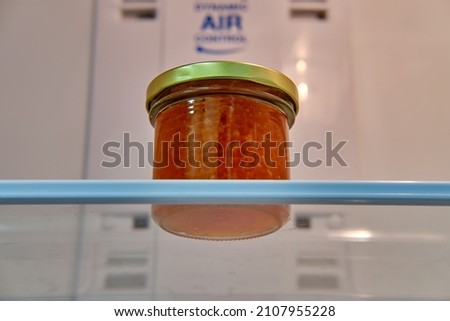 A jar of red caviar on a shelf in an empty white refrigerator