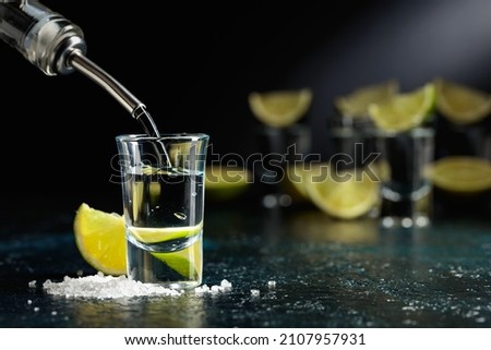 Tequila is poured into a glass. Tequila shots with lime slices and sea salt on a dark blue table. Royalty-Free Stock Photo #2107957931