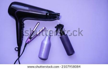 Hair dryer and hair straightener on a lilac background. Cosmetic models of bottles, tubes. The concept of beauty and care. Professional hairdressing equipment. Royalty-Free Stock Photo #2107958084