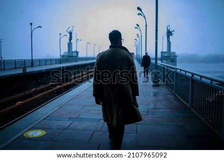 Back of cinematic young man in winter coat walking outside in urban city on bridge on a moody, foggy, winters night. Royalty-Free Stock Photo #2107965092