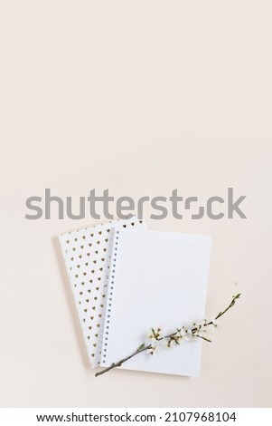 A blank notebook sheet with a sprig of white apple blossoms on a beige background with copy space