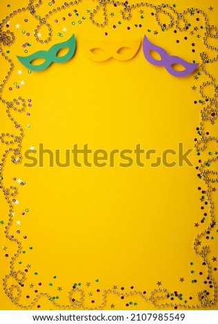 Mardi Gras gold color beads with Masquerade festival carnival masks and golden, green, purple confetti on yellow background. Party invitation, greeting card, venetian carnivale celebration concept.