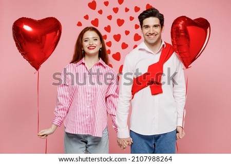 Young happy fun cheerful couple two friends woman man wear shirt hold red bunch of inflatable balloons isolated on plain pink background studio portrait. Valentine's Day birthday holiday party concept