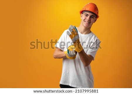 Confident smiling teen boy wearing orange hard hat against yellow background Royalty-Free Stock Photo #2107995881