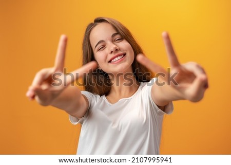 Young caucasian teen girl showing a peace symbol against yellow background