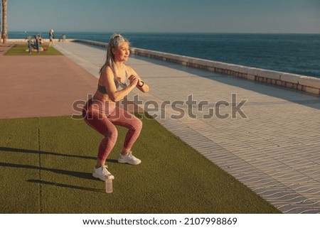 Active sporty woman performing squats on the sports street playground by the coast on warm sunny day Royalty-Free Stock Photo #2107998869