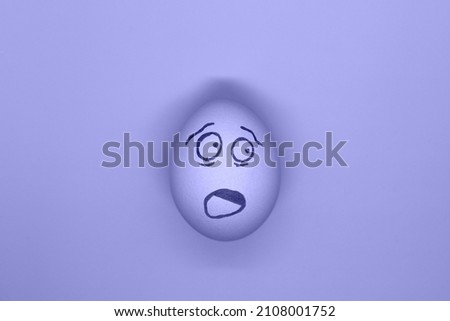 An egg with a painted face in the trending color of 2022 very peri, the concept of Easter