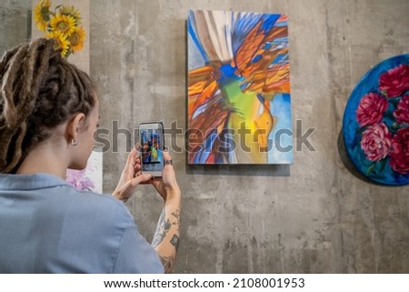 Contemporary young woman taking photo of abstract painting on wall while visiting exhibition in art gallery at leisure Royalty-Free Stock Photo #2108001953