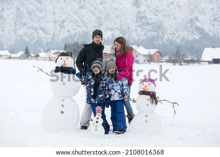 Family with children, building snowman in the park in little village in Austria, beuatiful landscape scenery