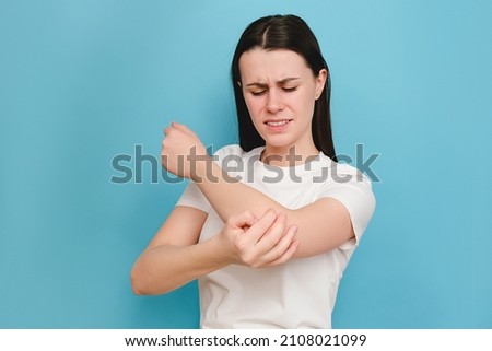 Unhappy sad young caucasian woman 20s old years having pain in his elbow, warming up injured hand after trauma, posing isolated over blue color background in studio with copy space for advertisement Royalty-Free Stock Photo #2108021099