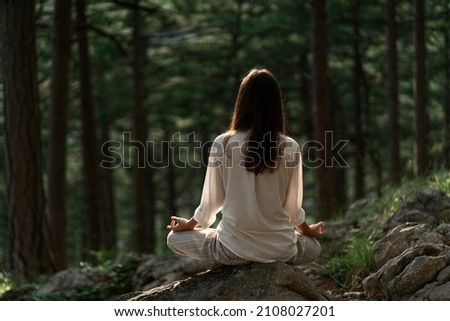 Beautiful young woman with long brunette hair meditates in nature, in a beautiful forest. Travel and healthy lifestyle, enjoying nature Royalty-Free Stock Photo #2108027201